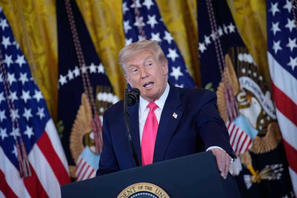 - Fotografía de Donald Trump durante un discurso en un acto oficial con banderas de EE.UU. de fondo, mostrando liderazgo y presencia política.