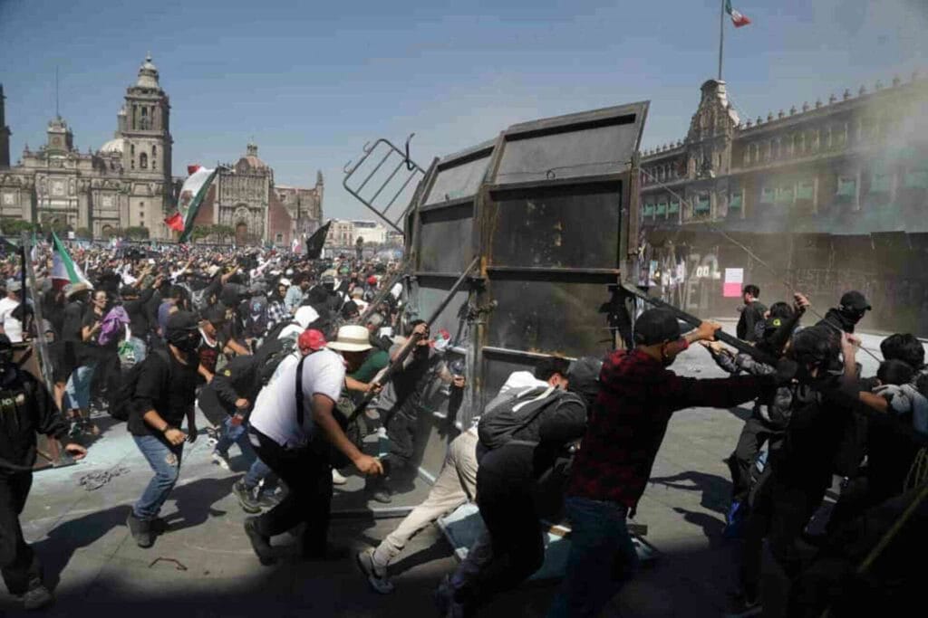 Manifestantes en protesta con barricadas y fuego en la calle frente a un edificio histórico en Ciudad de México, mostrando tensión social y movimientos políticos en el país.