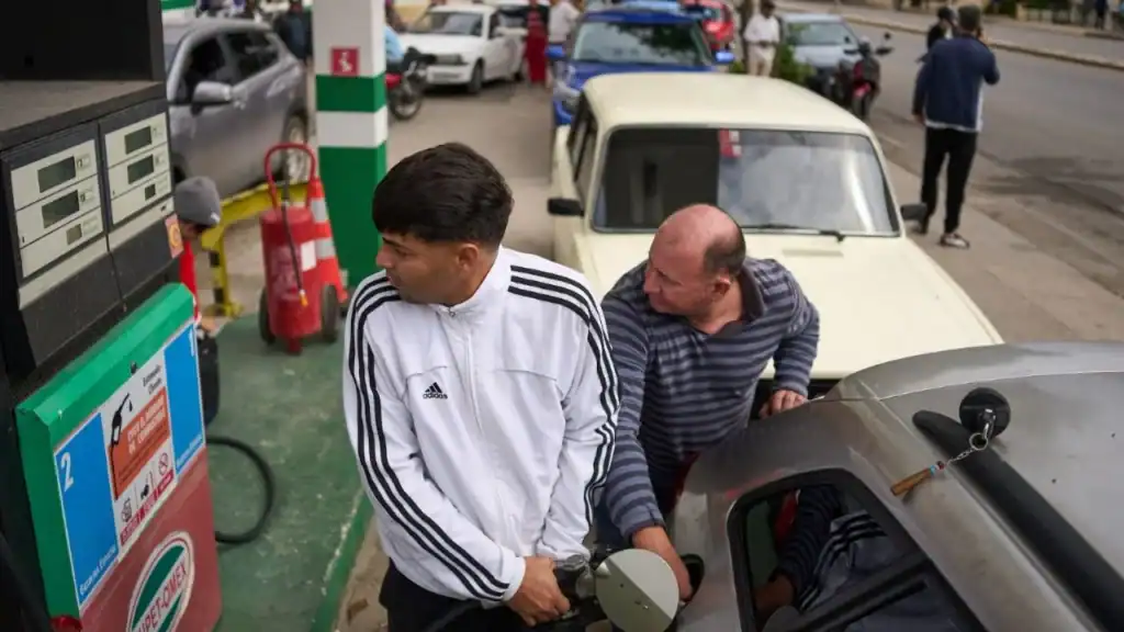 Personas repostan en una gasolinera mientras otros esperan detrás en una larga fila en La Habana, Cuba.