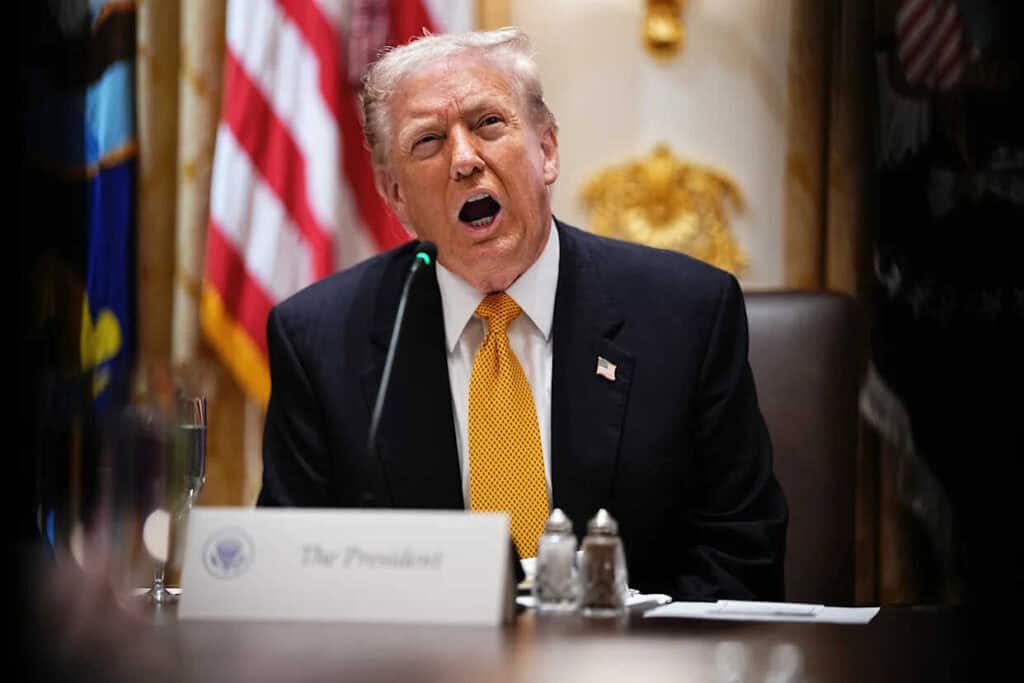 Donald Trump en una conferencia de prensa, con banderas de EE.UU. y decoraciones doradas en el fondo, mostrando una expresión facial de enojo o frustración durante un evento político importante.